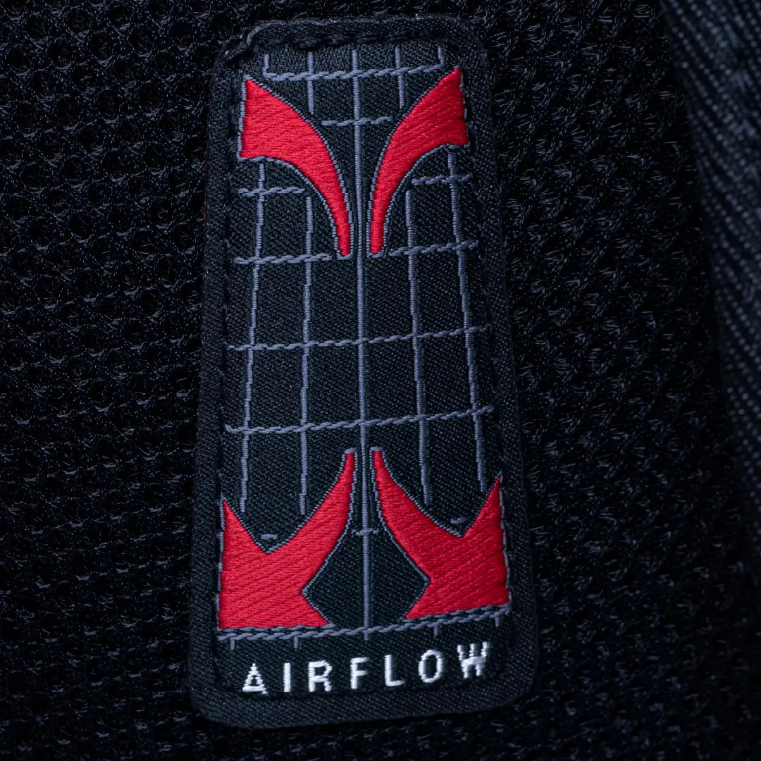 Close-up of a black mesh fabric patch with a red and gray grid design and the word AIRFLOW in white at the bottom.