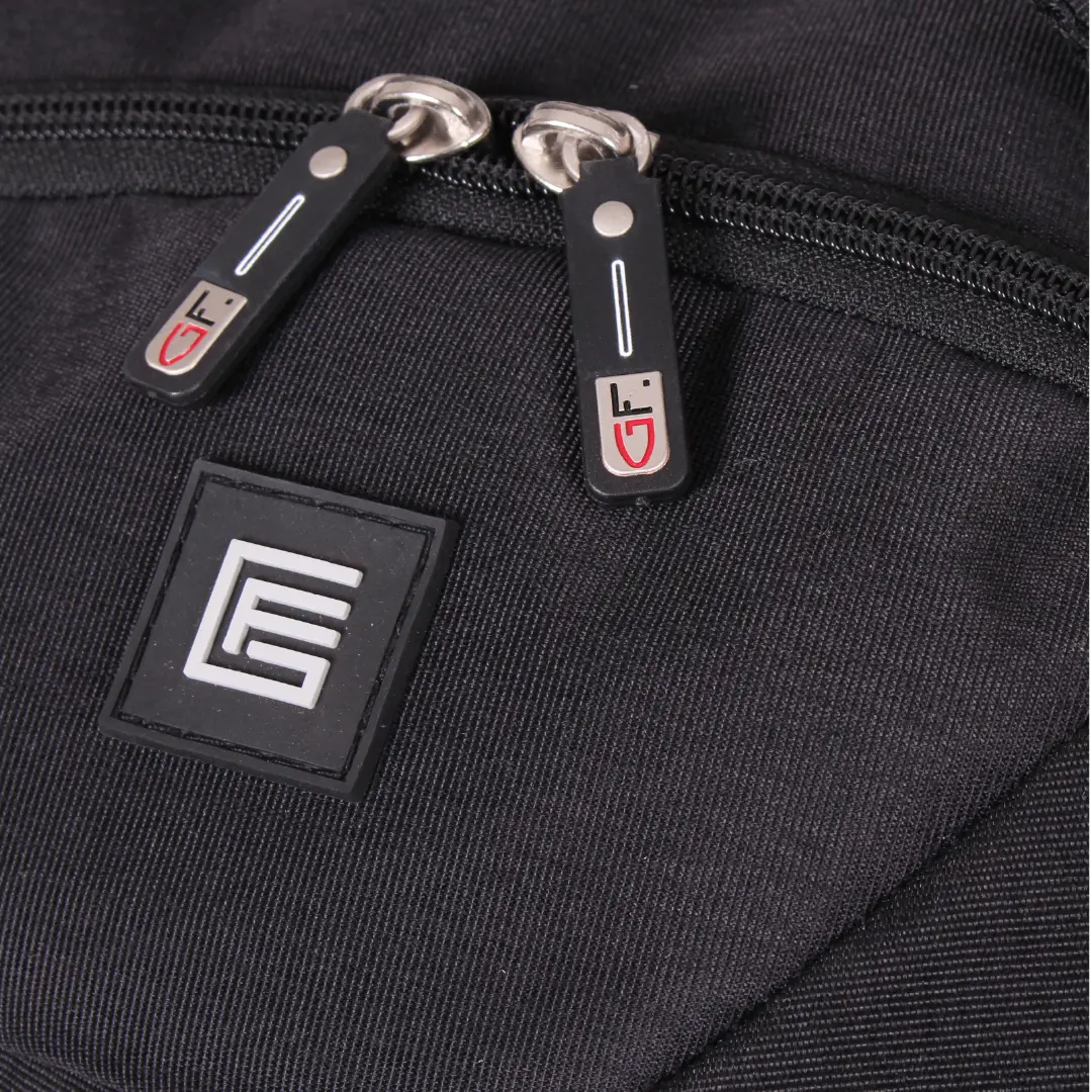 Close-up of a black fabric bag showing two black zipper pulls with silver metal rings and a square black patch featuring a white stylized logo.