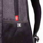 Close-up of a black and dark gray backpack showing the front mesh pocket, a black zipper, and a small red brand tag with a white bottle icon.