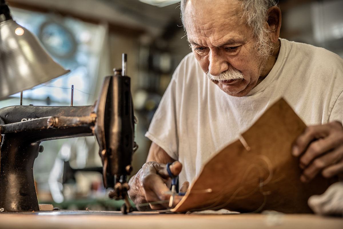 Man working with leather at a sewing machine in a workshop.
