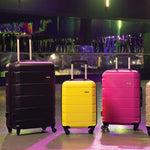 Four suitcases in black, yellow, pink, and beige on a reflective surface with a colorful background.