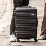 Black suitcase on wheels with a person's legs and feet in the background