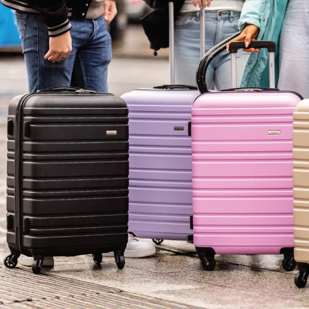 Four suitcases in black, purple, pink, and beige on a pavement.