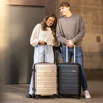 Two people with a beige and black suitcase standing in front of a building.