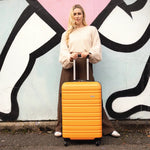 Woman holding a yellow suitcase against a colourful wall.