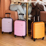 Three suitcases in purple, pink, and orange on a wooden floor with people sitting in the background.