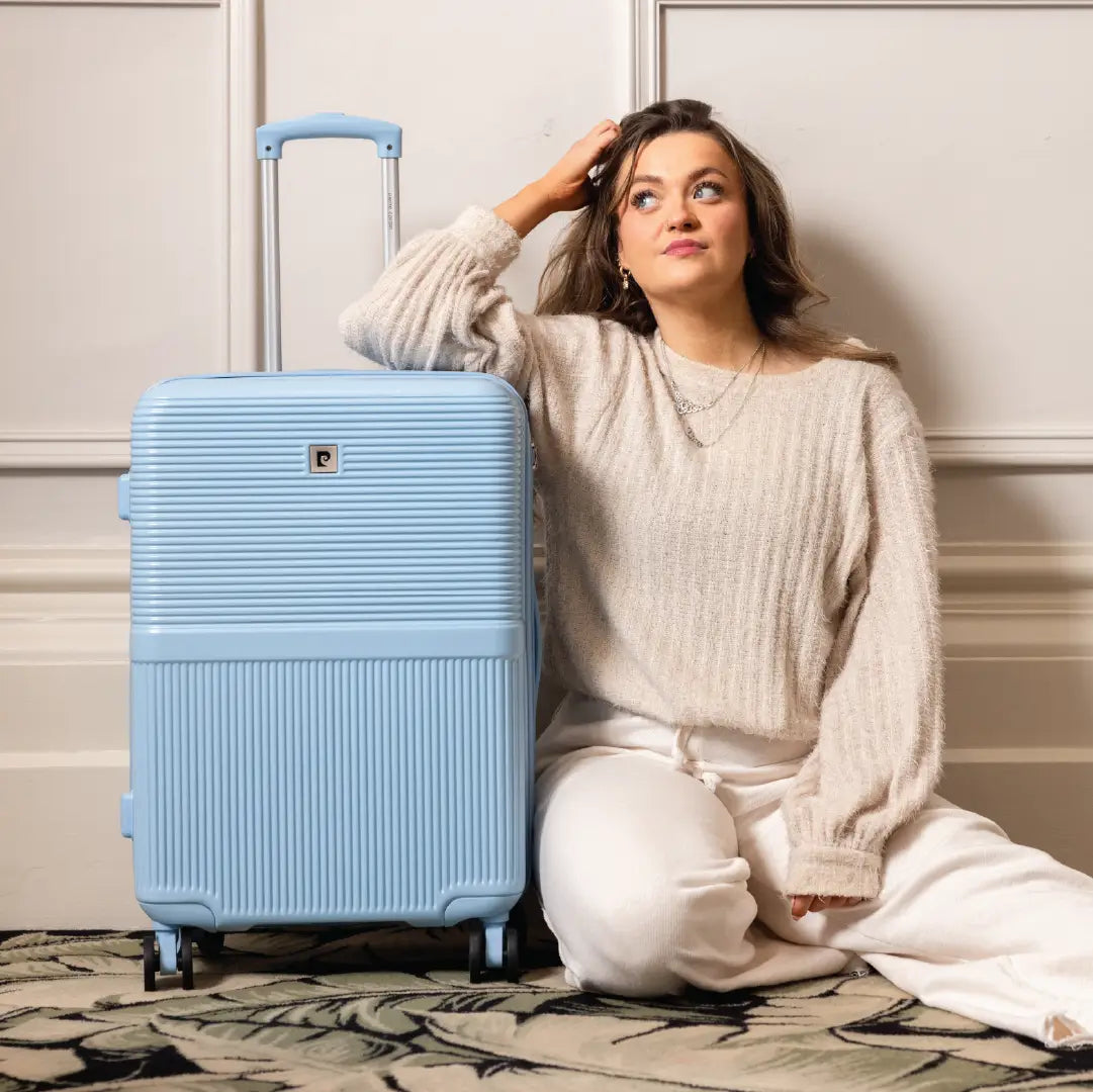 Woman sitting next to a light blue suitcase indoors