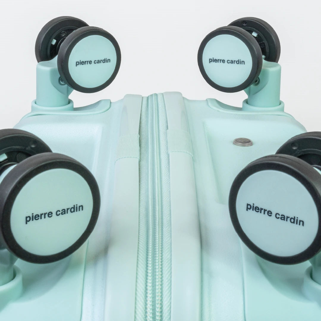 Light blue suitcase with 'Pierre Cardin' branding on wheels against a white background