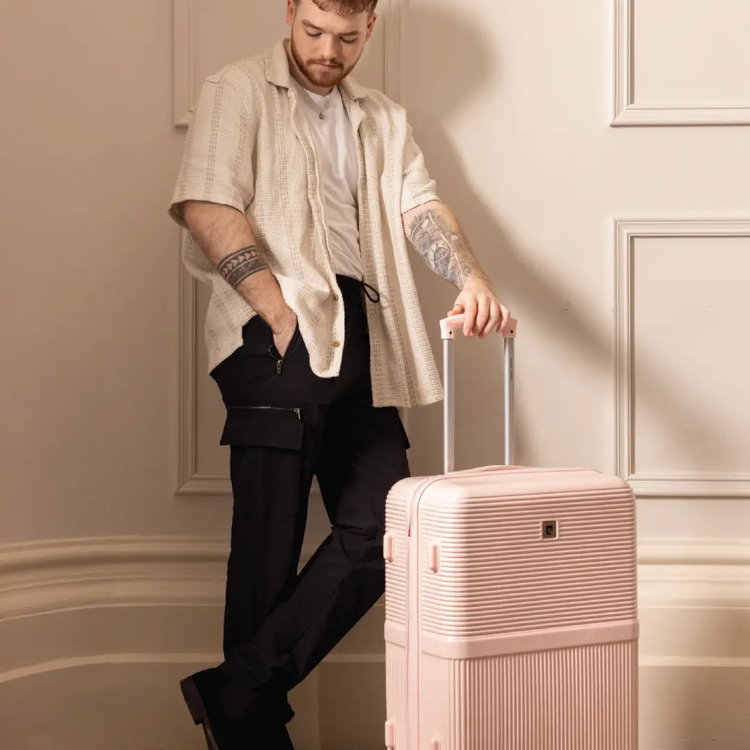 Man with tattoos holding a pink suitcase in an elegant interior setting