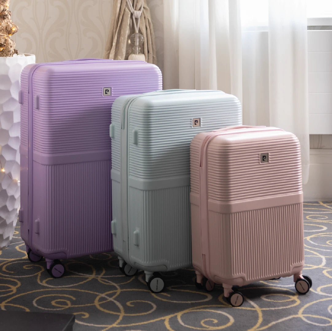 Three suitcases in purple, blue, and pink on a patterned carpet.