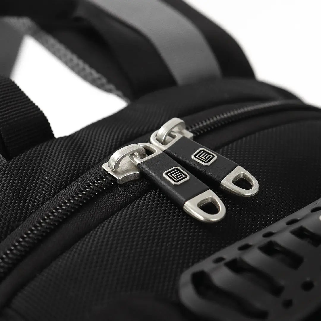 Close-up of a black textured nylon bag with dual silver metal zipper pulls featuring a black square logo.