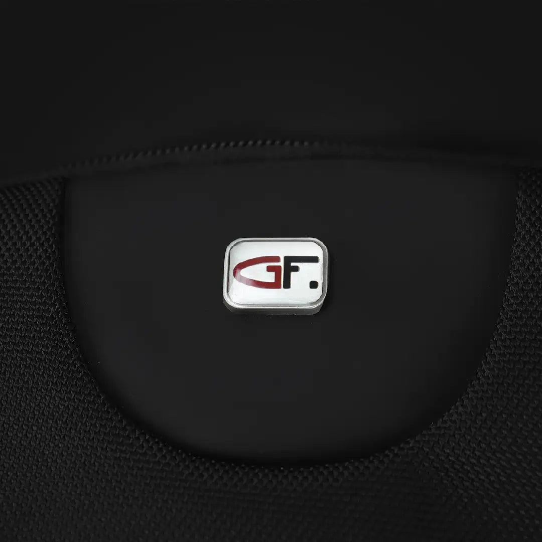 A close-up of a black textured fabric accessory featuring a central silver badge with a red and black stylized 'GF' logo.