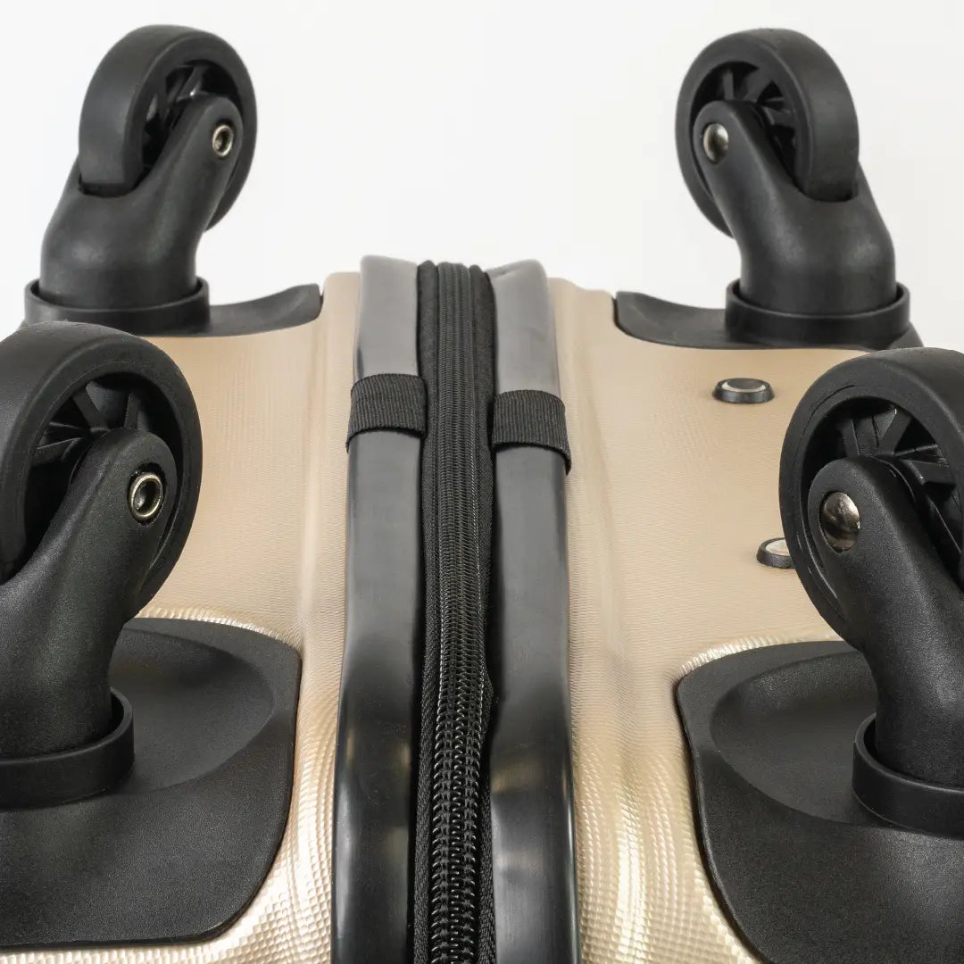 Close-up of gold hard-shell suitcase with a black wheels and a zip.