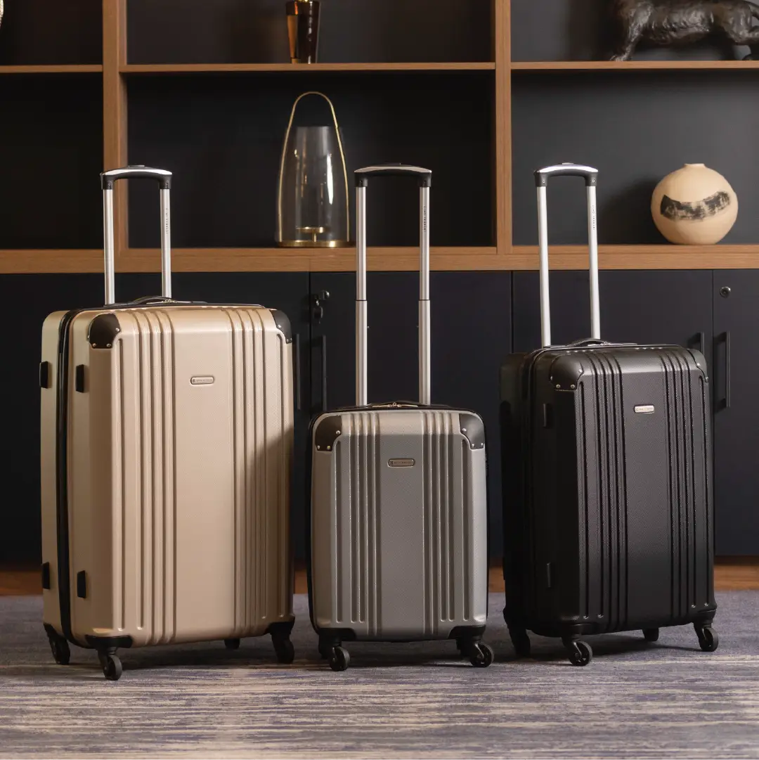 Three suitcases of different colors on a wooden floor with a dark wall and shelves in the background.