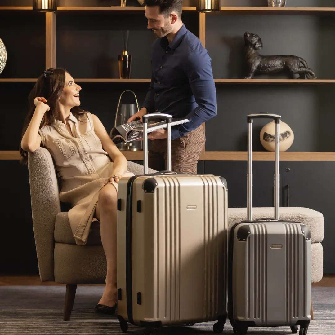 Man and Woman in a hotel with multiple gold hard-shell suitcases of different sizes.