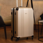 Gold hard-shell suitcase with a visible brand logo and black accents in a hotel reception setting.