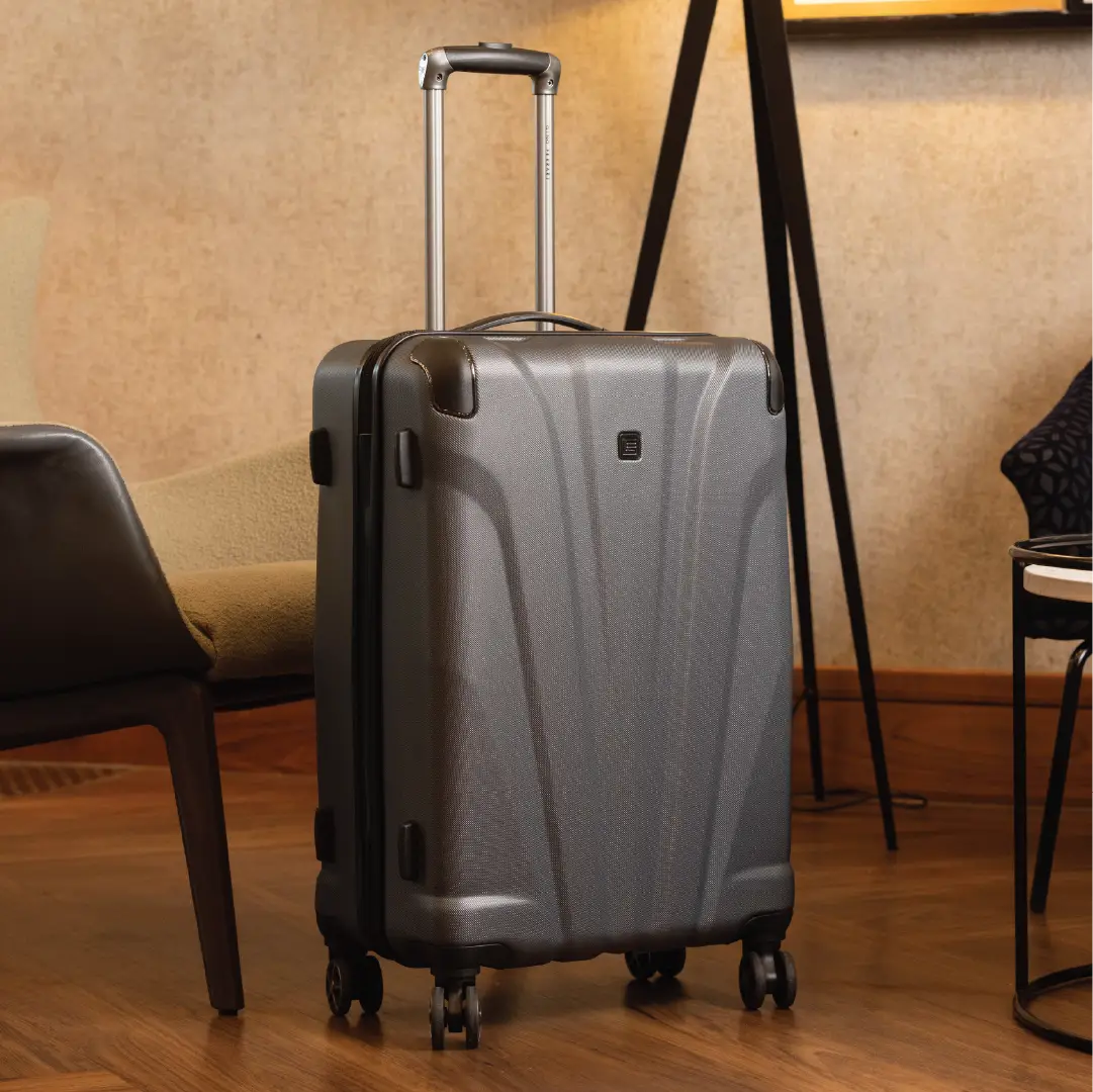 Silver suitcase on wheels in a room with chairs and a lamp.