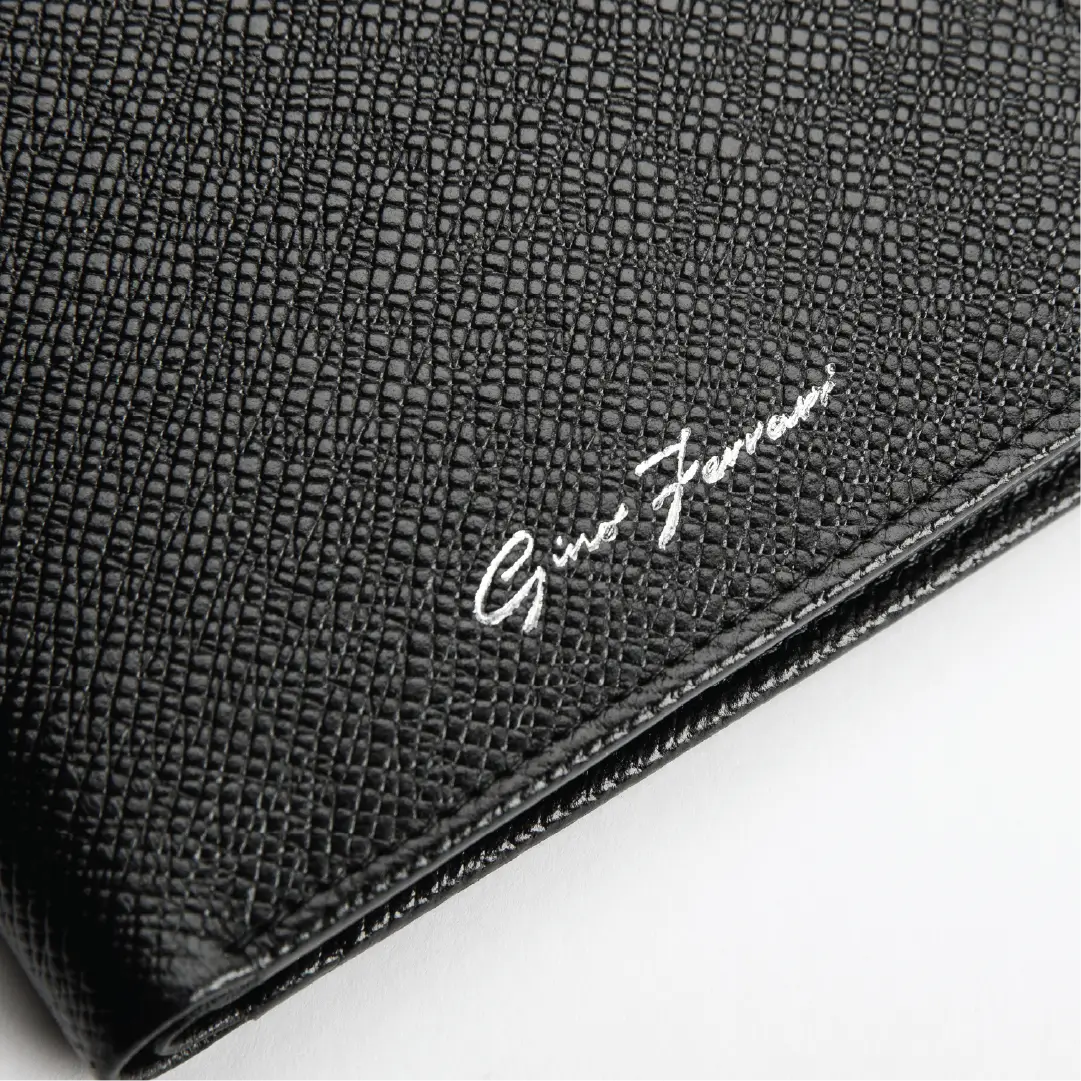 Close-up of a black textured leather clutch or wallet with a white script logo reading 'Gino Ferrari' on a white background.