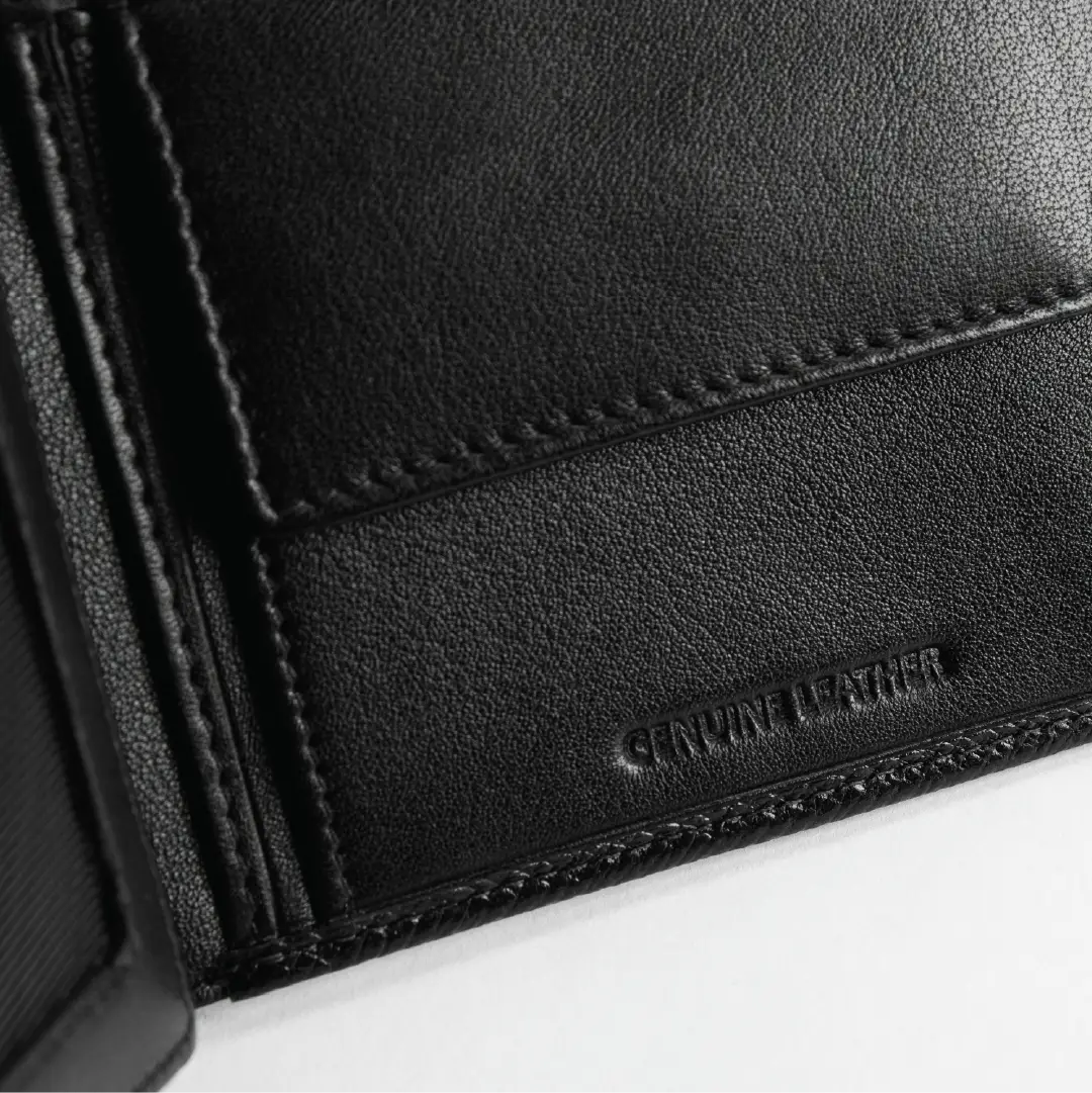 Close-up of a black genuine leather wallet or card holder showing stitched edges and embossed 'GENUINE LEATHER' text on a white background.