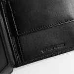 Close-up of a black genuine leather wallet or card holder showing stitched edges and embossed 'GENUINE LEATHER' text on a white background.
