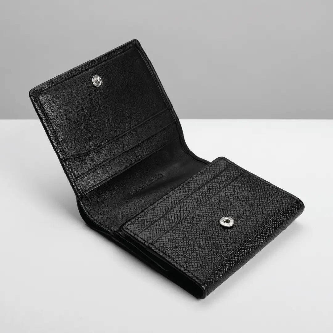 A black leather bi-fold wallet shown open, featuring a textured grain pattern on the front pocket and silver-tone snap buttons, set against a clean gray and white background.