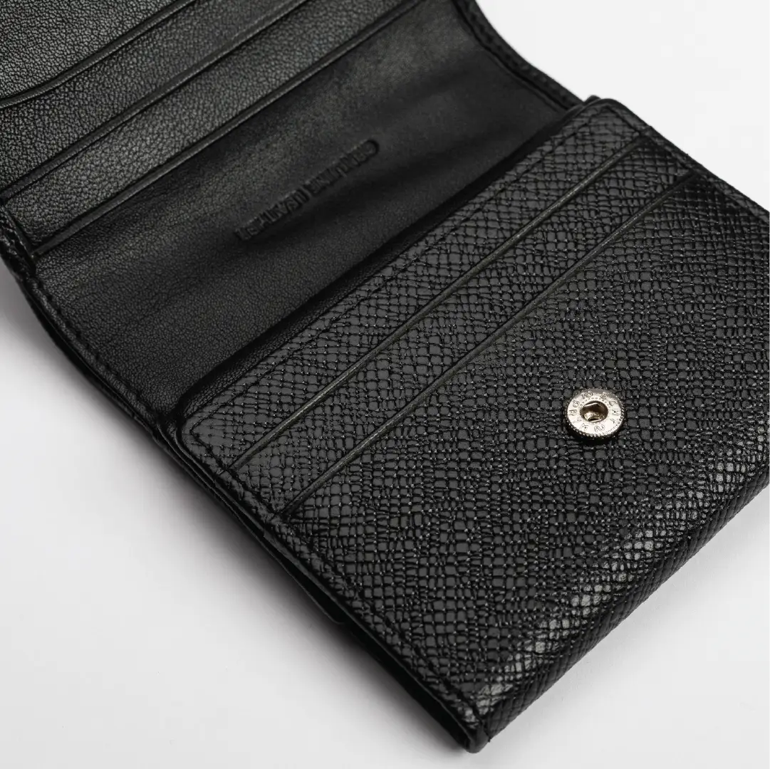 A close-up of an open black leather wallet with a textured exterior and a silver snap button closure is set against a plain light background.