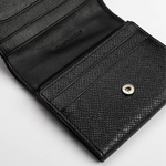 A close-up of an open black leather wallet with a textured exterior and a silver snap button closure is set against a plain light background.