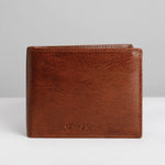 A brown leather bi-fold wallet with a subtle embossed logo on the front, photographed against a neutral light gray background.