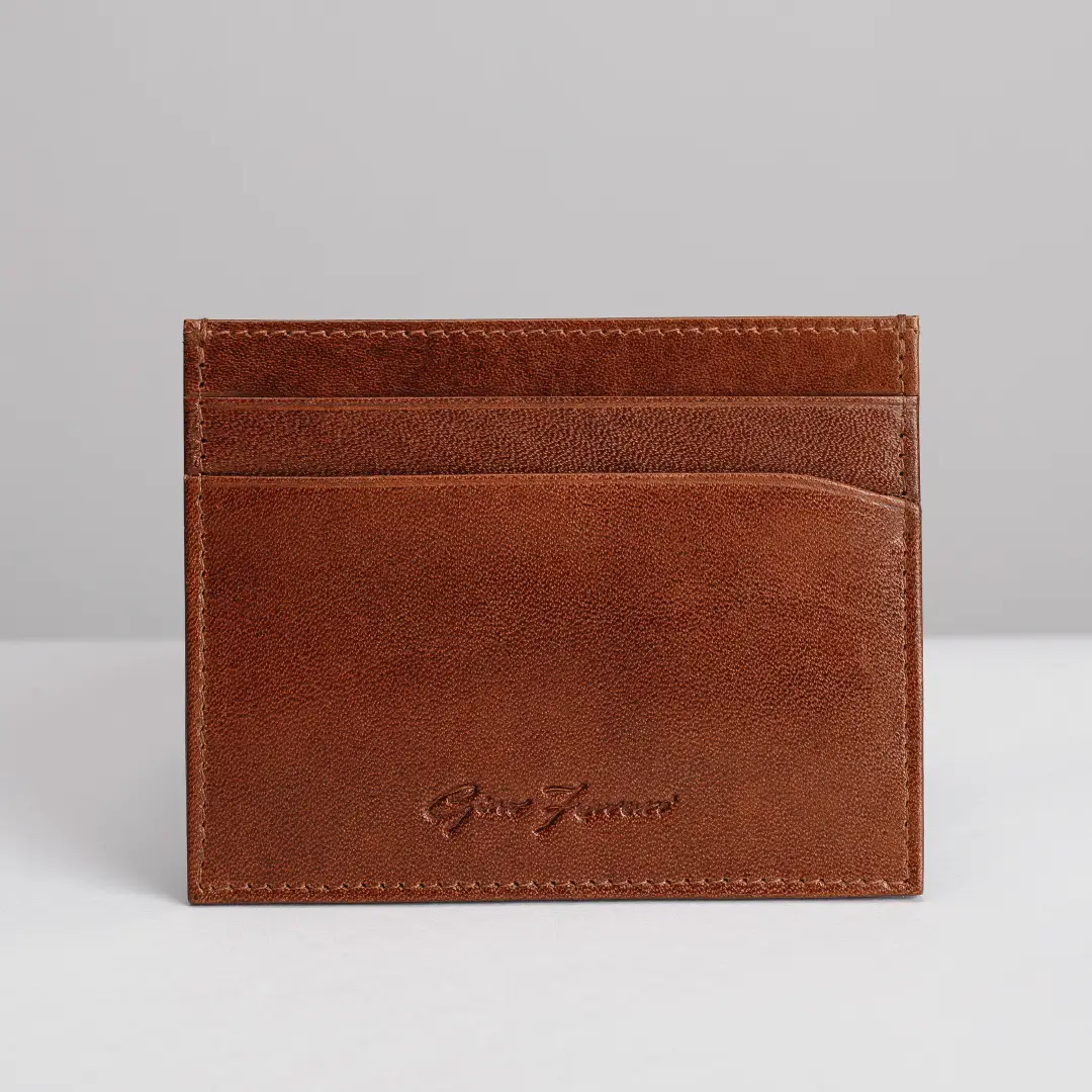 A brown leather card holder wallet with a debossed logo on the front, photographed against a neutral gray background.