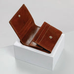 A brown leather bi-fold wallet shown open, resting on a white display block against a light gray studio background.
