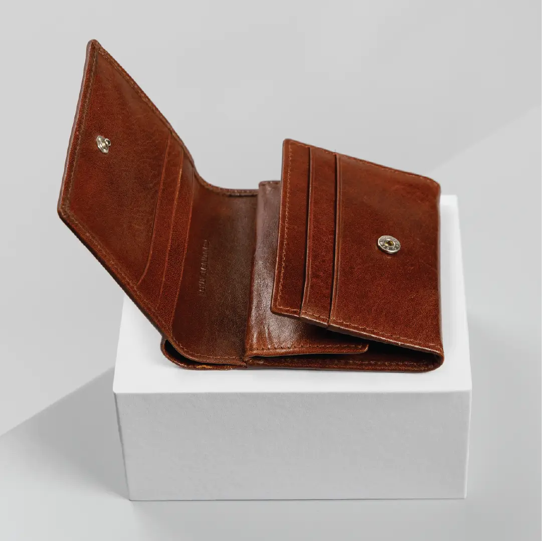 A brown leather bifold wallet with card slots and a snap-button closure, shown open on a white display block against a light gray background.