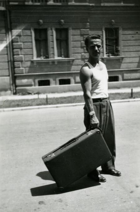 Man holding a suitcase on a street with a building in the background